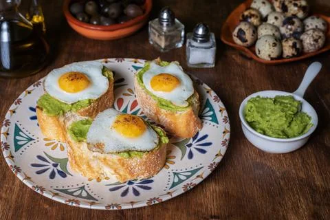 Slice of bread with avocado and grilled quail egg, on a wooden table. Stock Photos