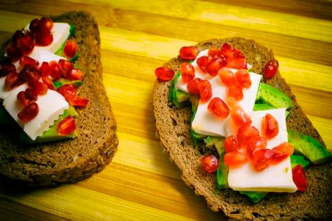 Slice of bread with avocado, cherry tomato, pomegranate seeds and fresh chees Stock Photos