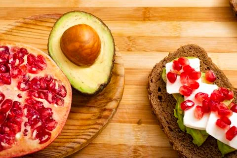 Slice of bread with avocado, cherry tomato, pomegranate seeds and fresh chees Stock Photos
