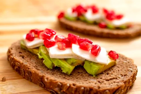 Slice of bread with avocado, cherry tomato, pomegranate seeds and fresh chees Stock Photos