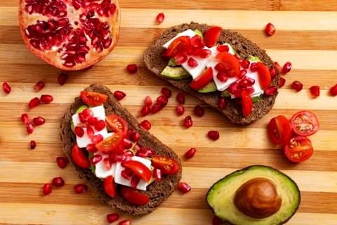 Slice of bread with avocado, cherry tomato, pomegranate seeds and fresh chees Stock Photos