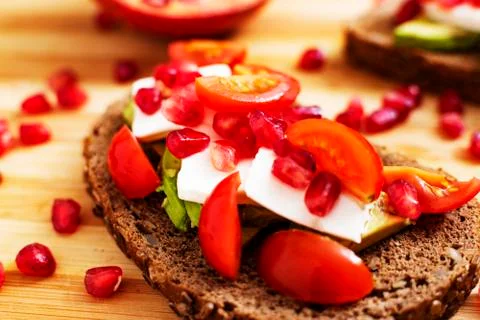 Slice of bread with avocado, cherry tomato, pomegranate seeds and fresh chees Stock Photos