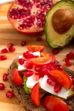 Slice of bread with avocado, cherry tomato, pomegranate seeds and fresh chees Stock Photos