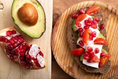 Slice of bread with avocado, cherry tomato, pomegranate seeds and fresh chees Stock Photos