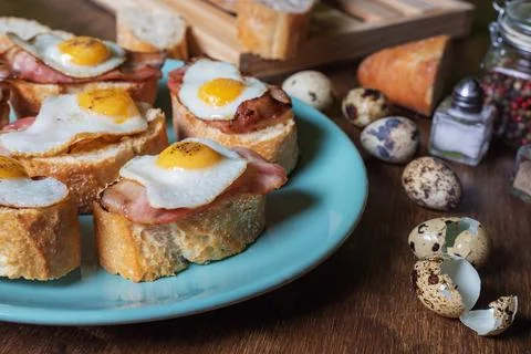 Slice of bread with bacon and grilled quail egg,on a wooden table. Stock Photos
