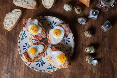 Slice of bread with bacon and grilled quail egg,on a wooden table. Stock Photos