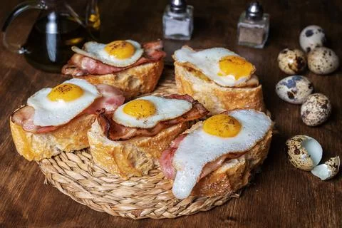 Slice of bread with bacon and grilled quail egg,on a wooden table. Stock Photos