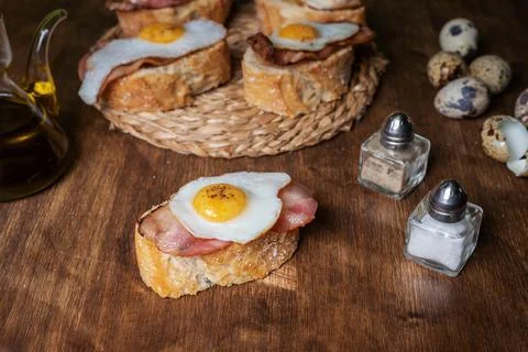 Slice of bread with bacon and grilled quail egg,on a wooden table. Stock Photos