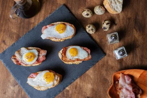 Slice of bread with bacon and grilled quail egg,on a wooden table. Foto stock