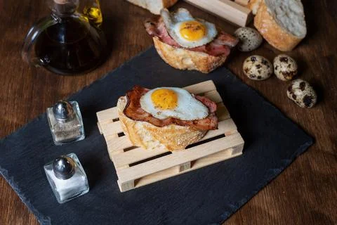 Slice of bread with bacon and grilled quail egg,on a wooden table. Stock Photos