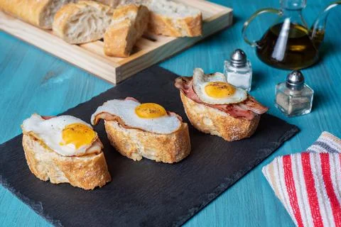 Slice of bread with bacon and grilled quail egg,on a wooden table. Stock Photos