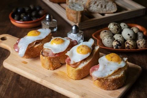 Slice of bread with bacon and grilled quail egg,on a wooden table. Stock Photos