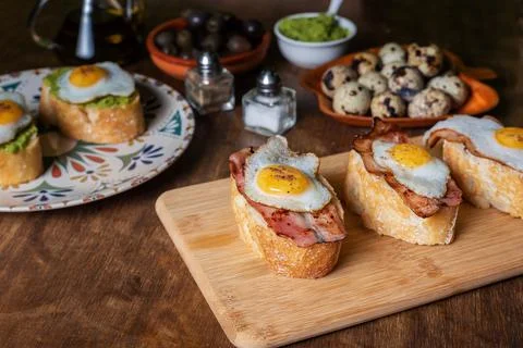 Slice of bread with bacon or avocado and grilled quail egg,on a wooden table. Stock Photos