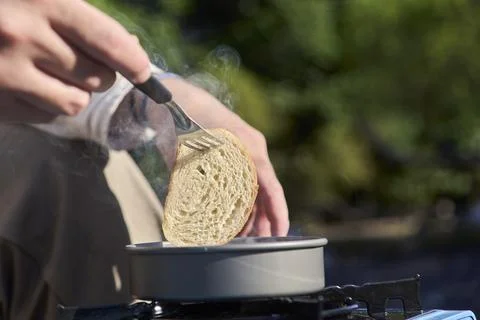 Slice of bread being lifted by an unknown person from a frying pan outdoors. Stock Photos