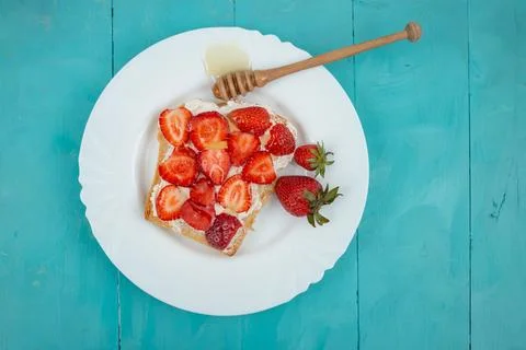 Slice of bread with cheese, strawberries and honey, on a white plate, on bl.. Foto stock