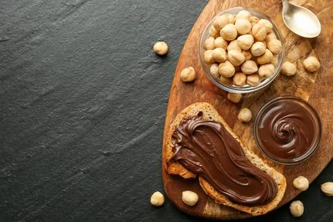 Slice of bread with chocolate spread and hazelnuts on dark textured table, .. Stock Photos