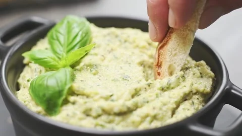 Slice of bread is dipping into roasted zucchini and tahini dip, slow motion. Stock Footage 153485389