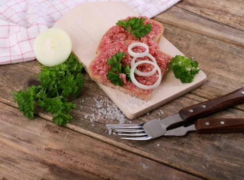 Slice of bread with minced meat, parsley and onions - on wooden table Stock Photos