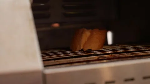 A slice of bread moves slowly along a conveyor toaster belt inside a breakfast Stock Footage 332416628