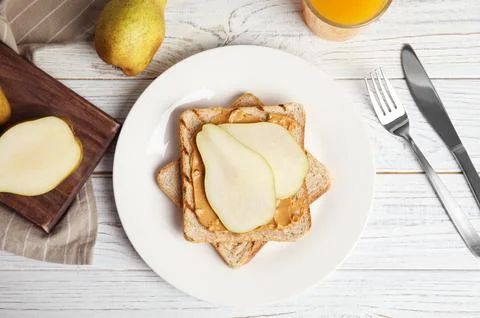 Slice of bread with peanut butter and pear on white wooden table, flat lay Stock Photos