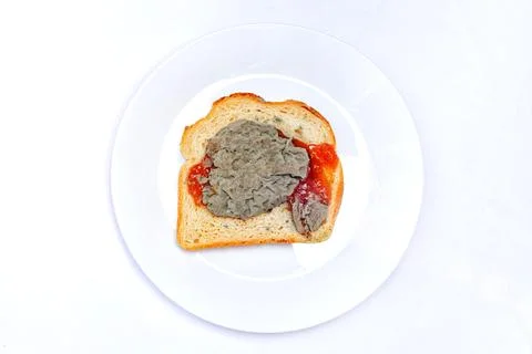 A slice of bread sits on a white plate topped with a grey spread and red sauc Stock Photos