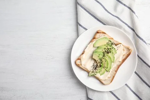 Slice of bread with spread and avocado on white wooden table, flat lay. Space Stock Photos