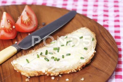 A slice of bread spread with butter and chives on wooden plate Stock Photos