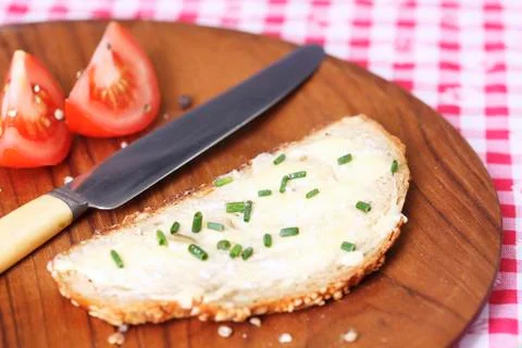 A slice of bread spread with butter and chives on wooden plate Stock Photos