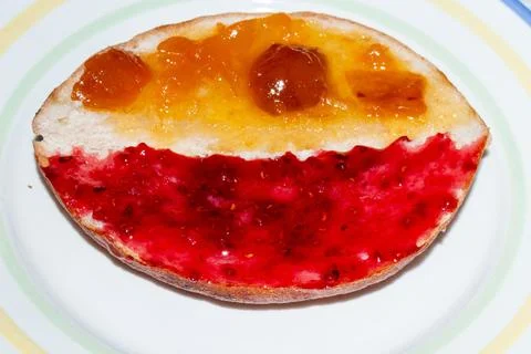 A slice of bread with strawberry jam and apricot preserve on a white plate Stock Photos