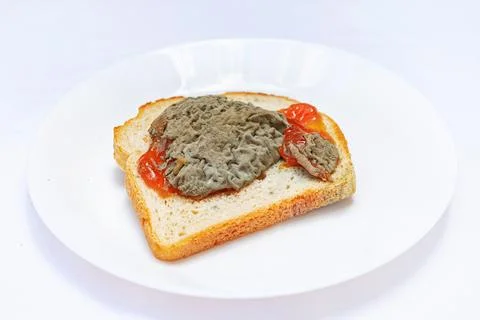 A slice of bread topped with a gray spread and a red condiment sits on a whit Stock Photos