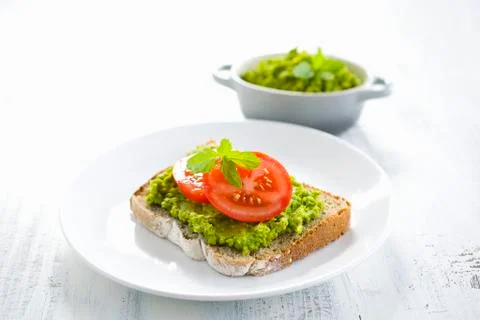 A slice of bread topped with a pea spread and tomatoes Stock Photos