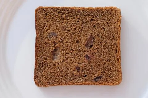 Slice of brown bread with raisins on a white plate top view. A square slice o Stock Photos