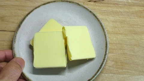 A slice of butter is cut into small pieces and placed on a white plate. Stock Footage 318009523
