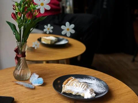 Slice of cake is on a plate in front of a vase of flowers Stock Photos