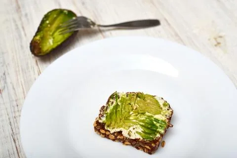 Slice of cereal bread with cream cheese and avocado on a white plate. Vegetar Stock Photos