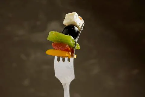 Slice of cheese with olive and pepper on a fork, dark mood Stock Photos