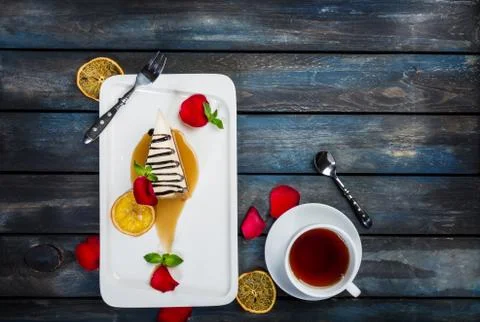 Slice of Cheesecake with a cup of tea on a white plate with rose petals. Top Foto stock