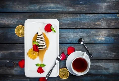 Slice of Cheesecake with a cup of tea on a white plate with rose petals. Top 스톡 사진