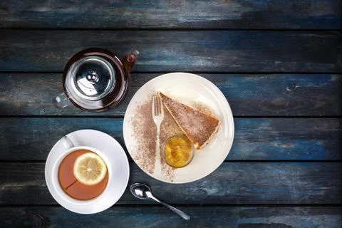 Slice of Cheesecake with jam and tea kettle with lemon on a colored wooden ba Stock Photos