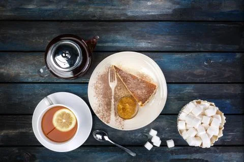 Slice of Cheesecake with jam and tea kettle with lemon and rafinated sugar on Stock Photos