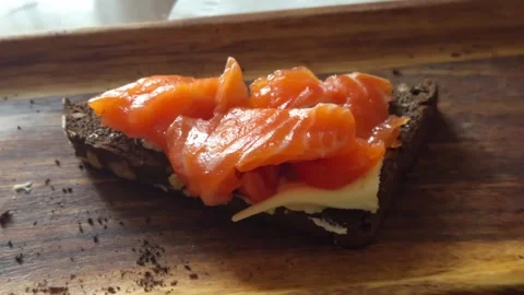 A slice of dark bread with butter and pieces of red fish served on a wooden.. Stock Footage 319443072