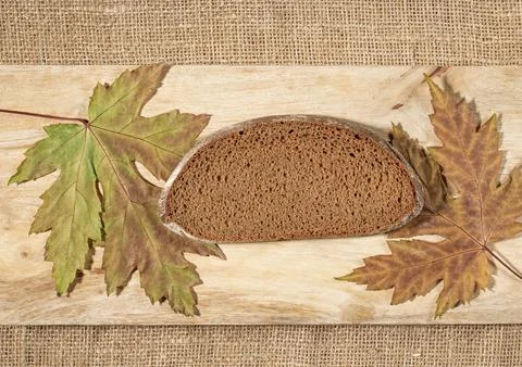 A slice of dark rye peasant bread on a texture board surrounded by maple leaves Stock Photos