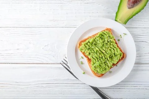A slice of fresh bread on a plate with avocado on a background of light wooden Stock Photos
