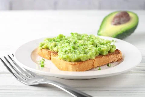 A slice of fresh bread on a plate with avocado on a background of light wooden Stock Photos