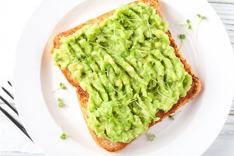 A slice of fresh bread on a plate with avocado on a background of light wooden Stock Photos
