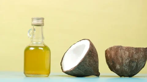 Slice of fresh coconut and bottle of oil on against yellow background Stock Footage 202022865