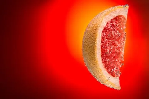 Slice of grapefruit in water covered with bubbles on gradient fiery red bac.. Stock Photos