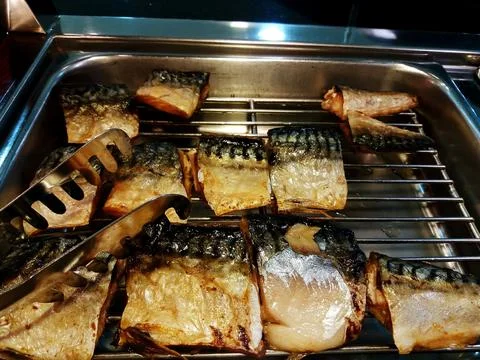 Slice of grilled and fried saba on steel grate tray of food with tongs. Fotos de archivo