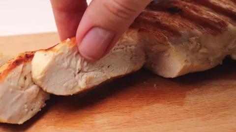 Slice the grilled chicken breast with a knife on a wooden chopping board Stock Footage 296972171