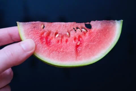 A slice of juicy fresh mini watermelon in a female hand on a dark background. Stock Photos